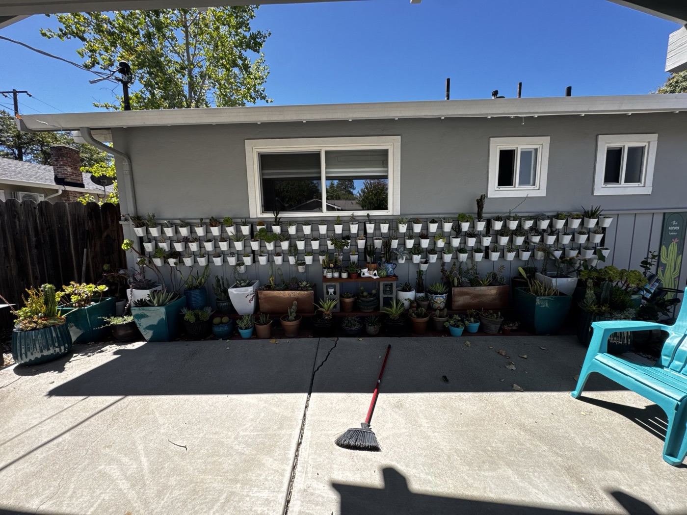 The full wall of white cups on the gray house, with a row of potted plants and a wooden bench along the base.